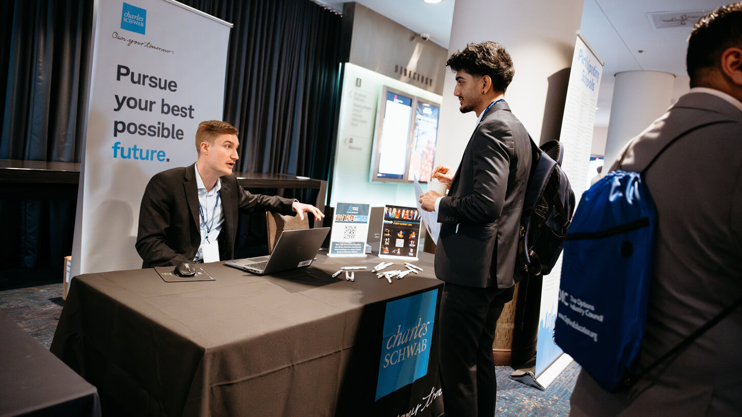 A Charles Schwab recruiter discusses internship or career opportunities with a student at a career fair table.