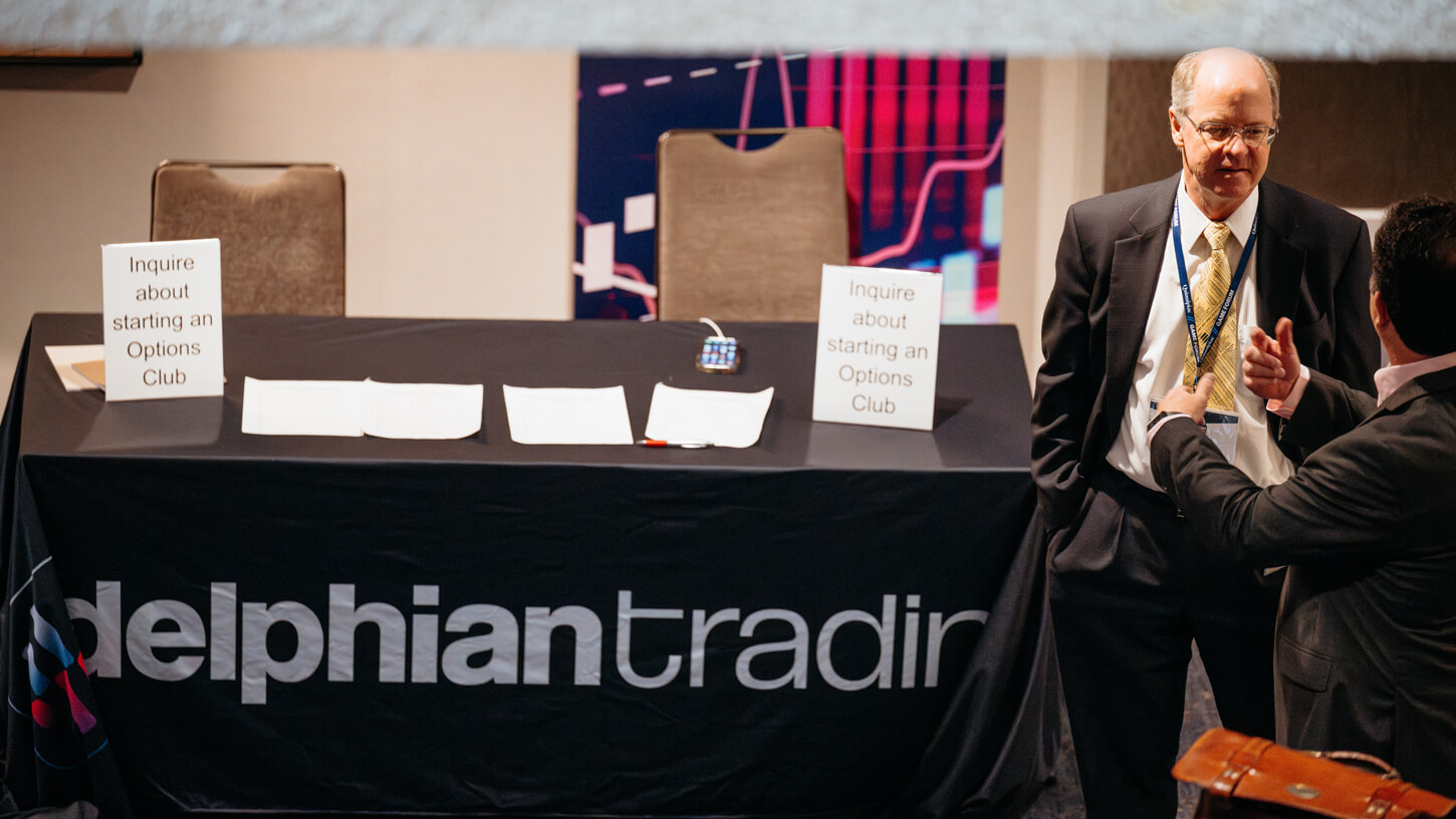 A Delphian Trading expert chats with an attendee next to signage encouraging options club formation.