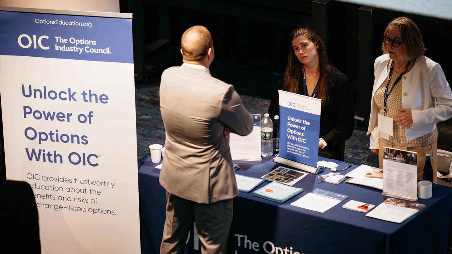 Representatives from the Options Industry Council speak with a guest in front of an exhibit display about listed options.