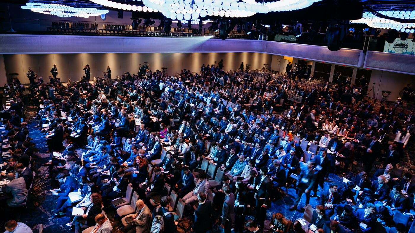 A packed auditorium of students and professionals attending the Quinnipiac GAME Forum, seated under glowing blue ceiling lights.