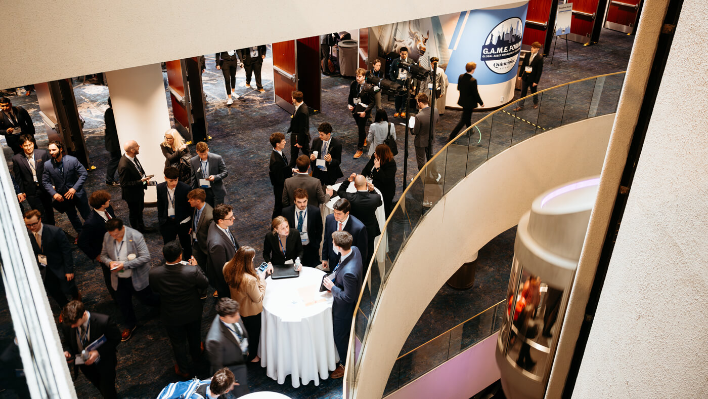 Overhead view of students and professionals networking in a busy atrium during the GAME Forum, near the event’s branding display.