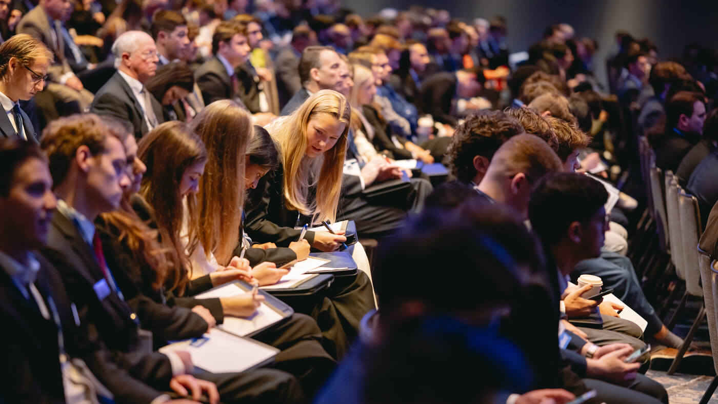 Rows of students in business attire focus on taking notes during a presentation at the GAME Forum.