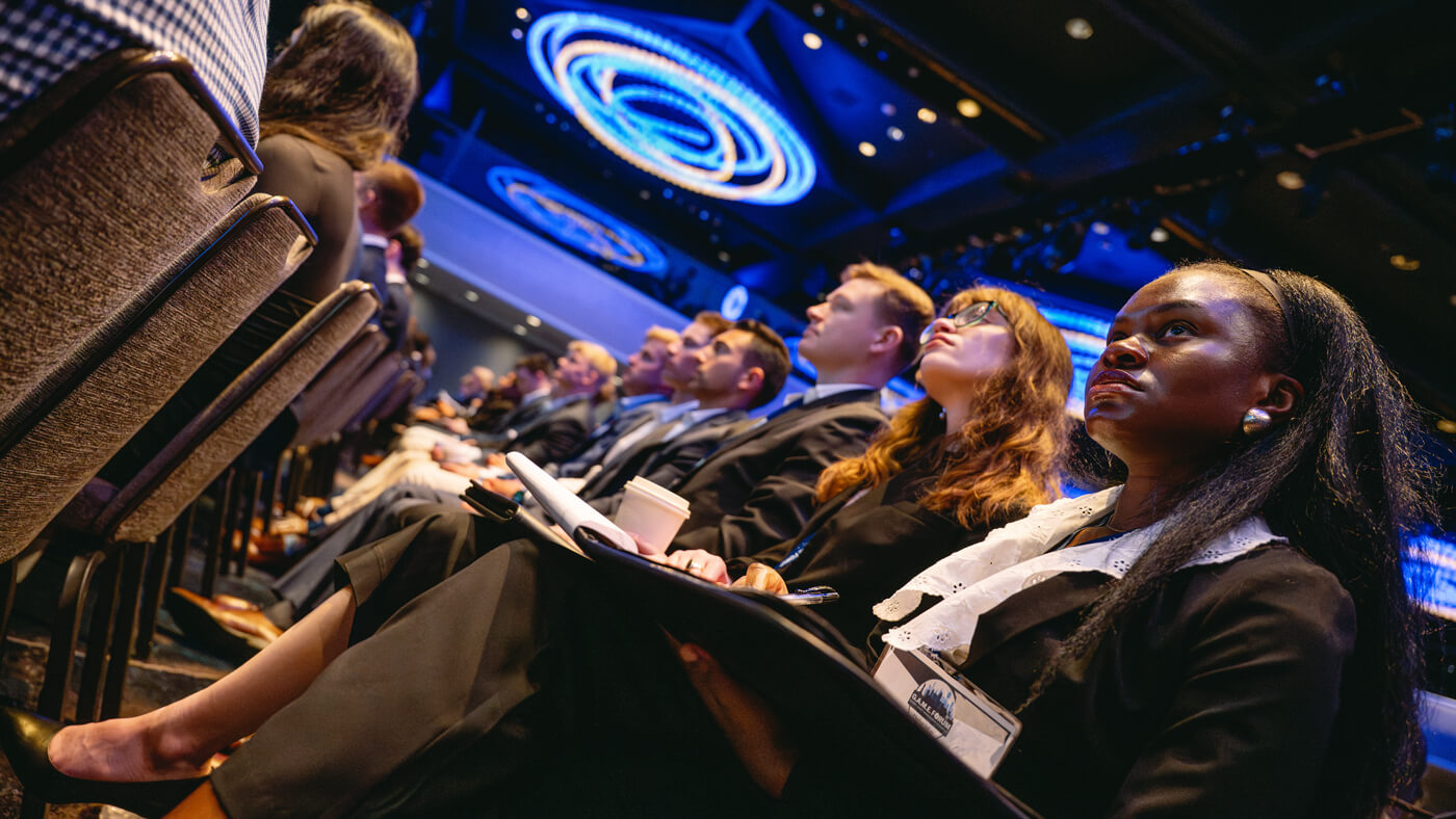 A group of students sit in a front row, looking forward with focus during a session at the GAME Forum.