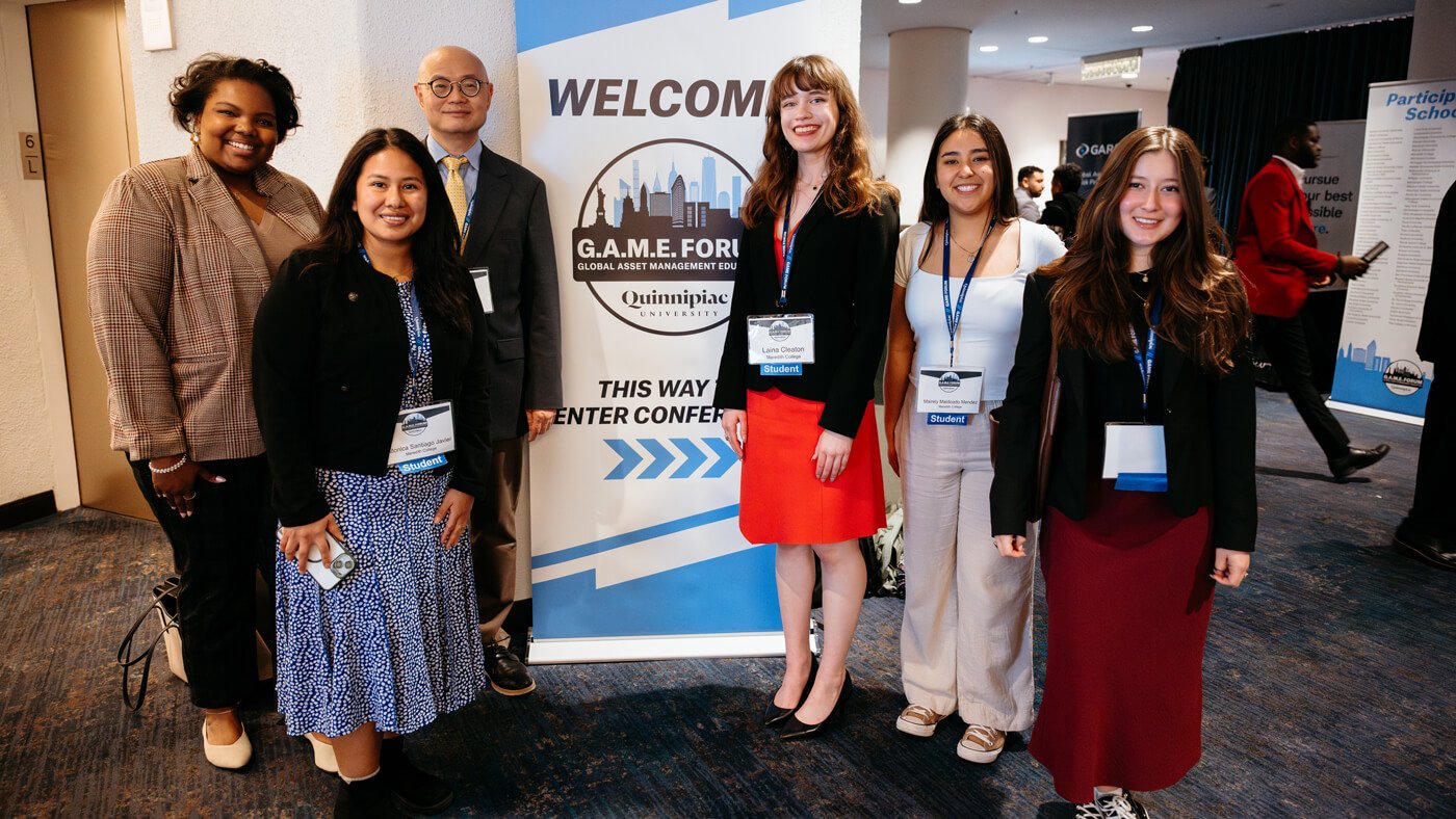 Student participants pose for a group photo beside a “Welcome to G.A.M.E. Forum” sign inside the conference venue.