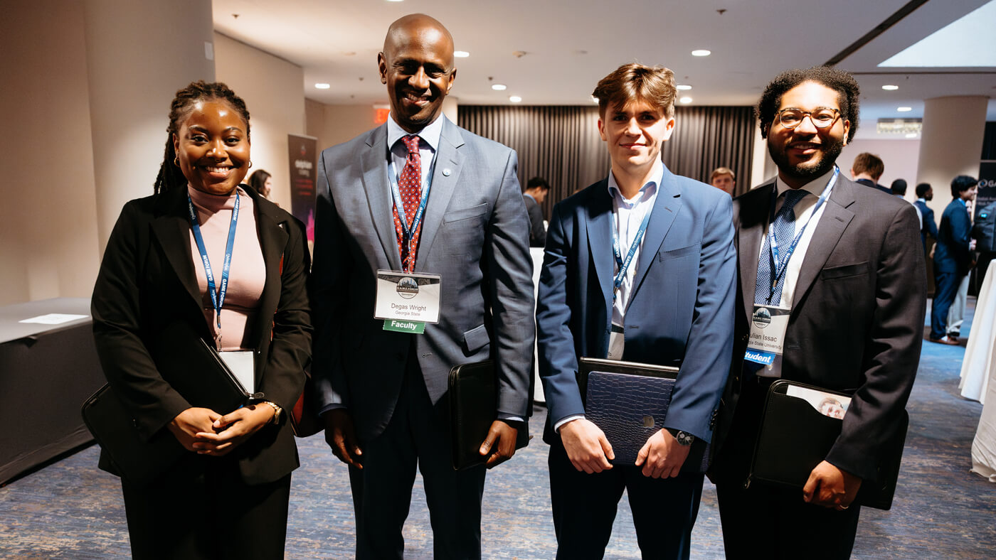 Four attendees pose together at the forum, including faculty and students, smiling in professional attire.