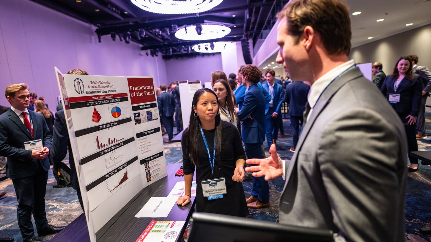A student from Trinity University discusses her team’s “Framework of the Fund” poster, which includes investment strategy, guest speakers, and diversification charts.